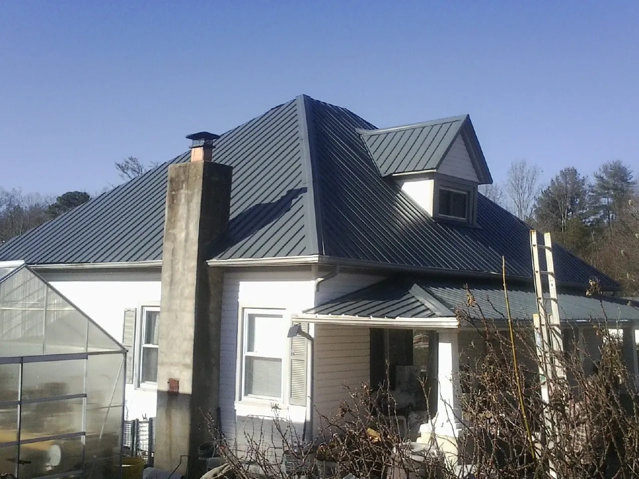 Dark blue standing seam metal roof on a white farmhouse with dormer — Slate & Tile Roof Repair by Roofing Brothers in Cliffwood