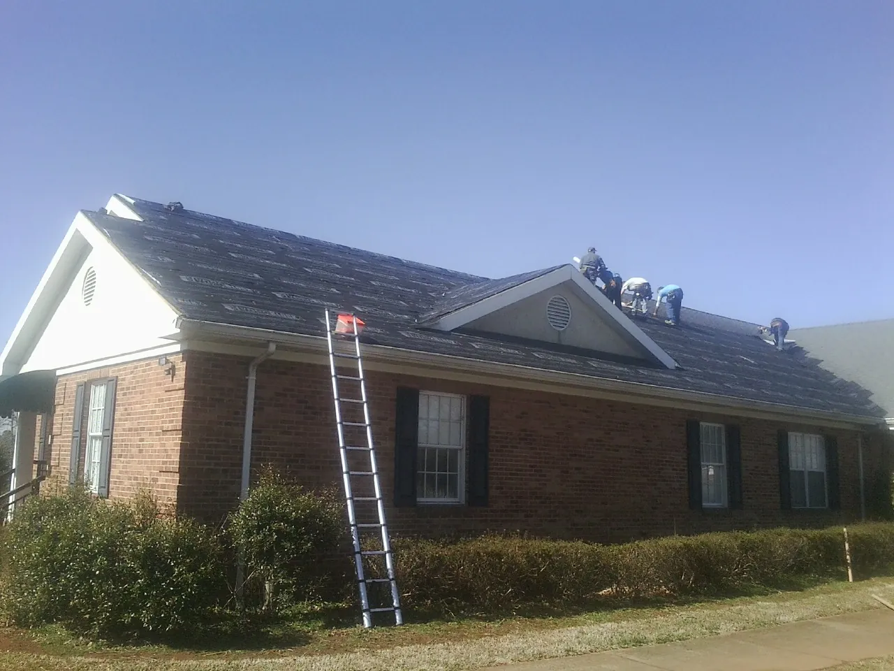 Crew tearing shingles off a brick ranch roof with a ladder set — Emergency Roof Repair work by our crew in Cliffwood