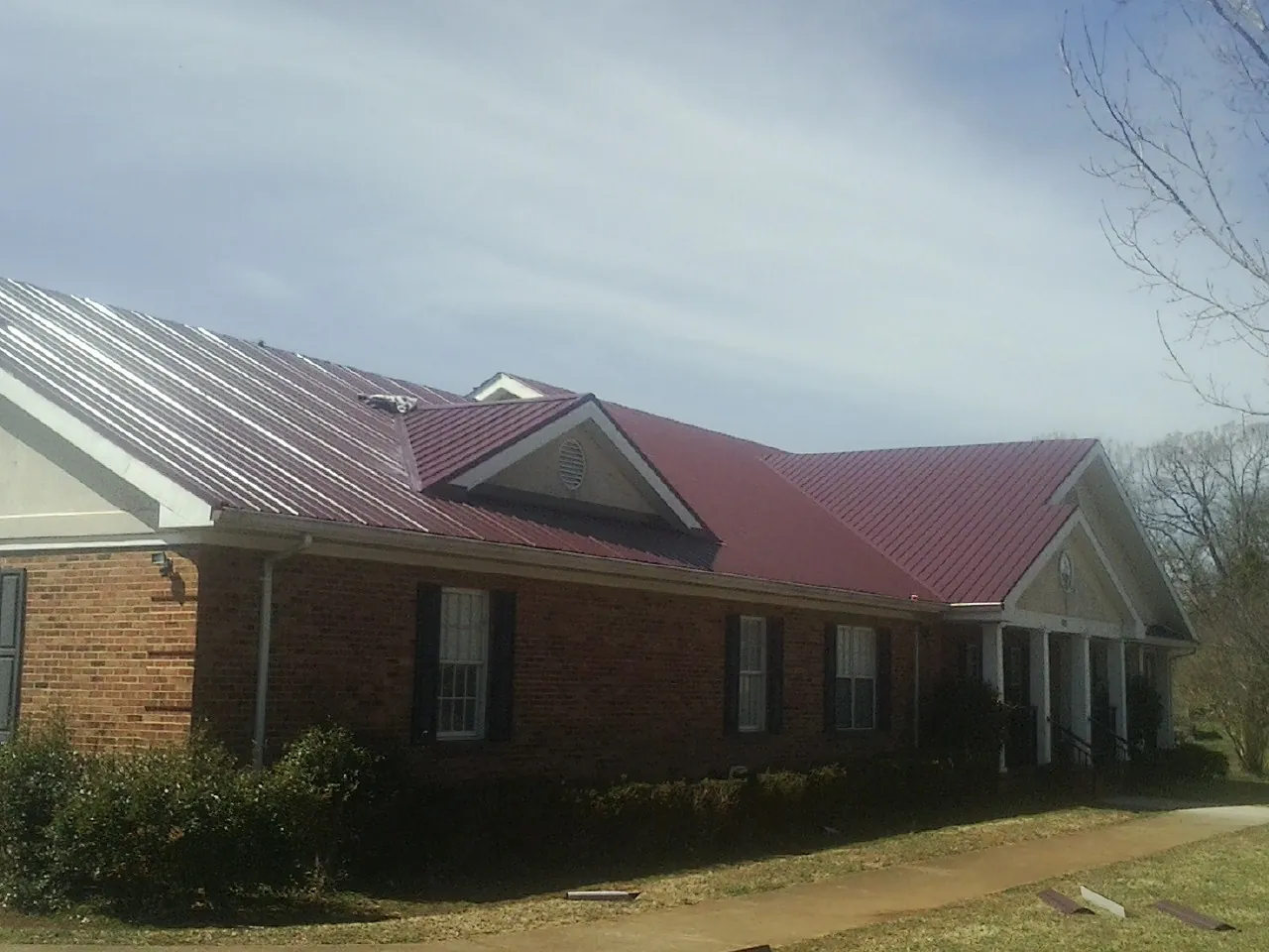 Red metal roof with gabled entries on a long brick building, from a Hail Damage Roof Repair job in Cliffwood