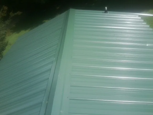 New green metal panels meeting at the ridge of a roof — Flat Roof Repair work by our crew in Cliffwood