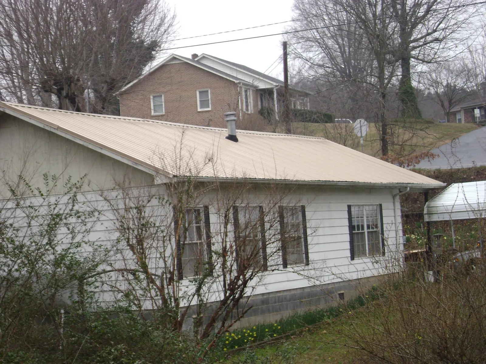 Tan metal roof on a white sided house set into a hillside — Commercial Roofing by Roofing Brothers in Cliffwood
